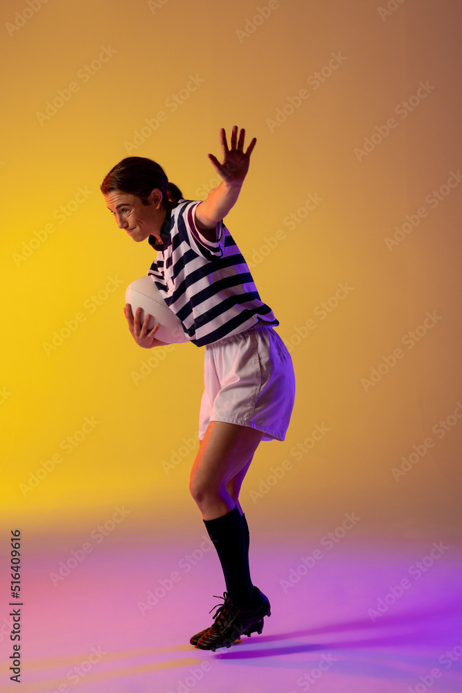 Caucasian female rugby player with rugby ball over neon pink lighting