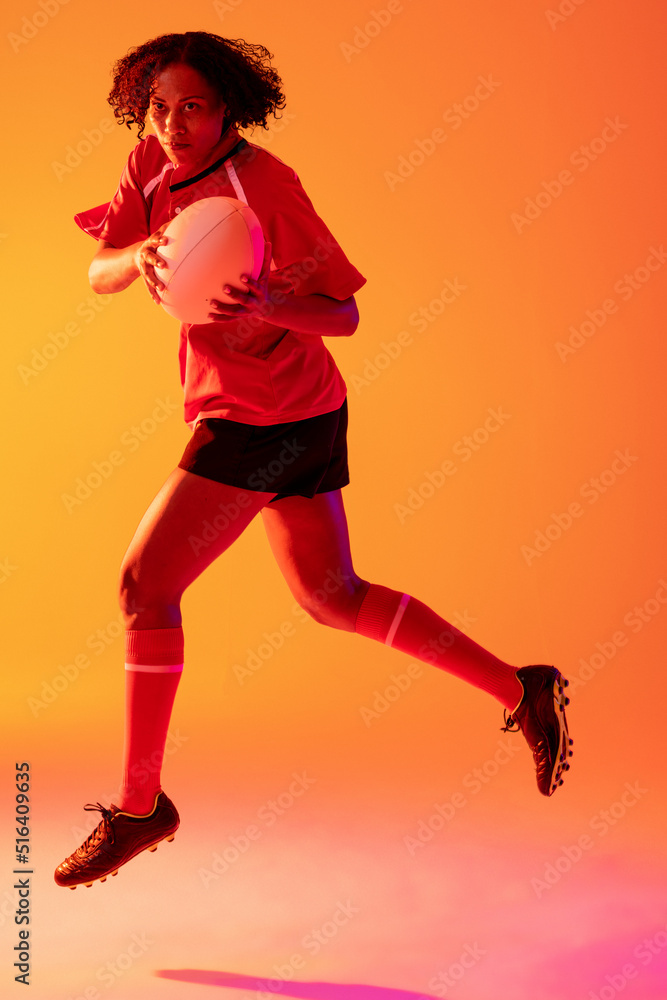 African american female rugby player with rugby ball over neon pink lighting