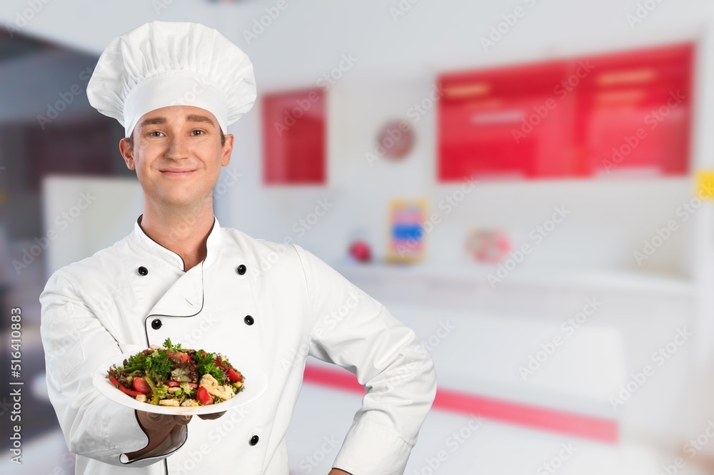 Young man standing and holding plate or dish on kitchen background