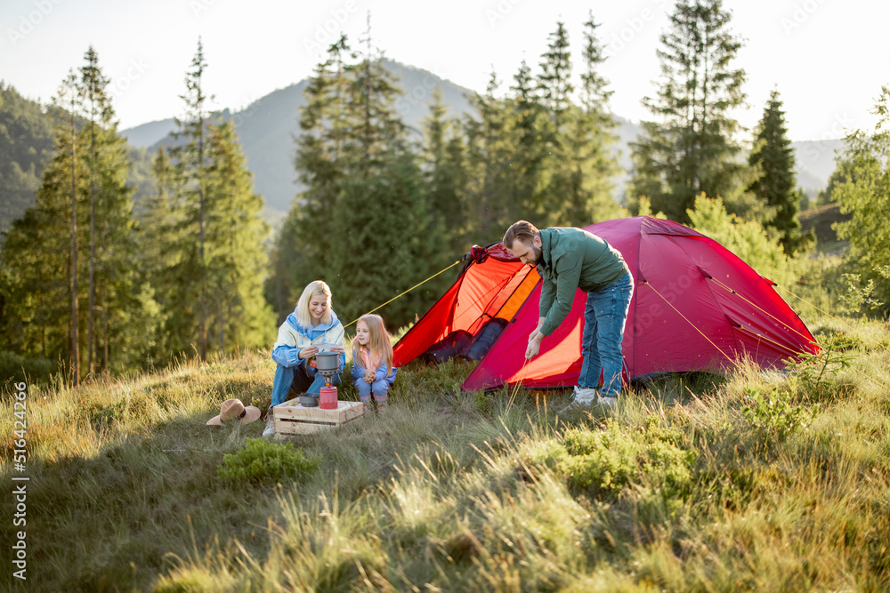 Couple with little girl have picnic at campsite while traveling with tent in the mountains. Young fa