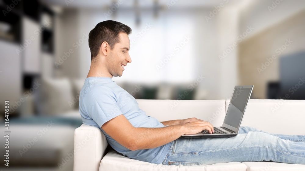 Portrait of smiling man using laptop. Adult male sitting on comfy couch in living room, watching vid