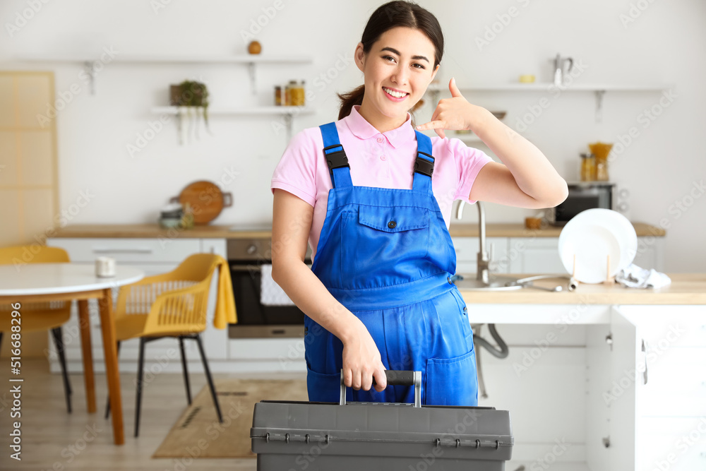 Asian female plumber holding bag with tools in kitchen