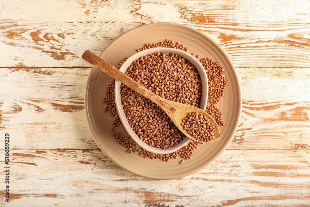 Plates and spoon with buckwheat grains on light wooden background