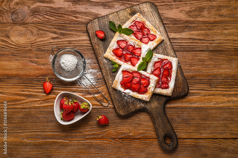 Delicious strawberry puff pastry and sieve with sugar powder on wooden background