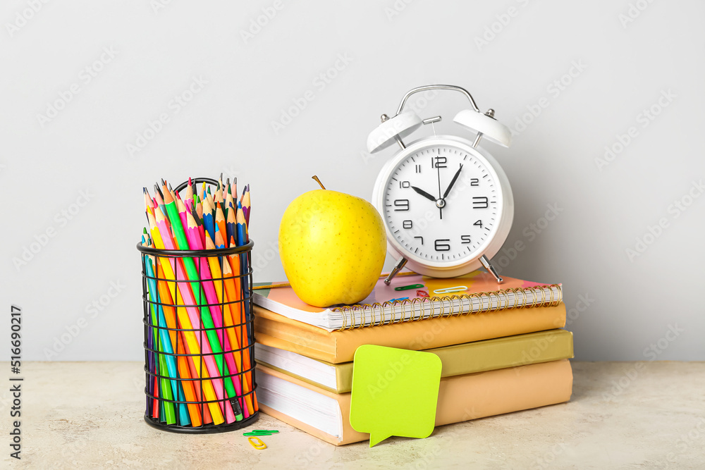 School stationery with apple and alarm clock on table against grey background