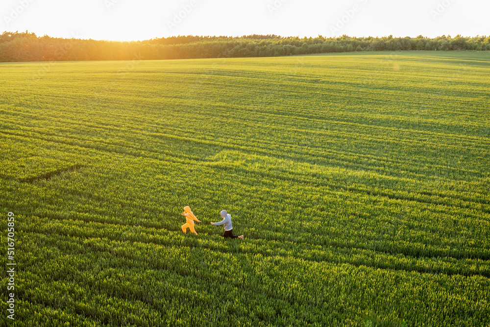 Aerial view on green wheat field with couple walking on pathway on sunset. People enjoy nature on fa