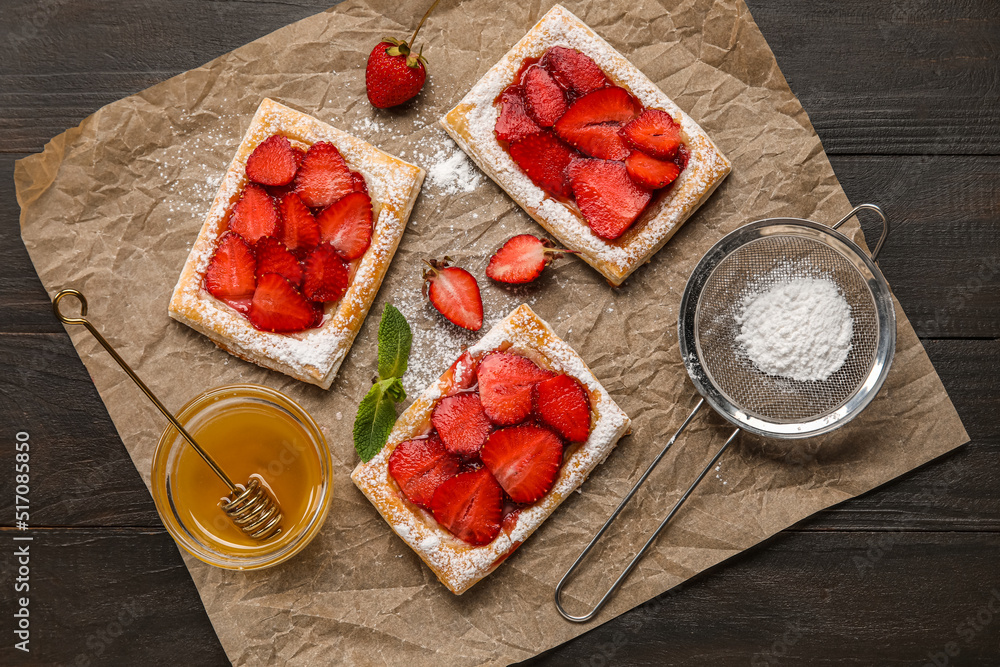 Delicious strawberry puff pastry, bowl with honey and sugar powder on dark wooden background