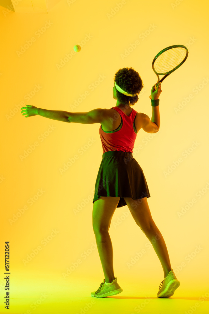 Vertical image of back view of african american female tennis player in yellow lighting