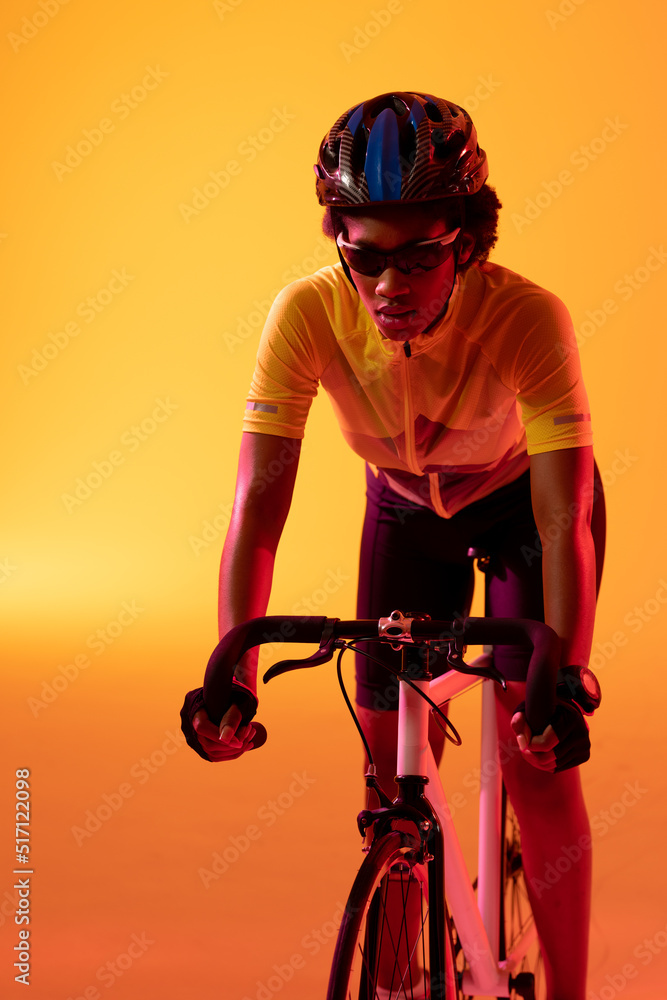 Vertical image of african american female cyclist riding bike in neon orange lighting