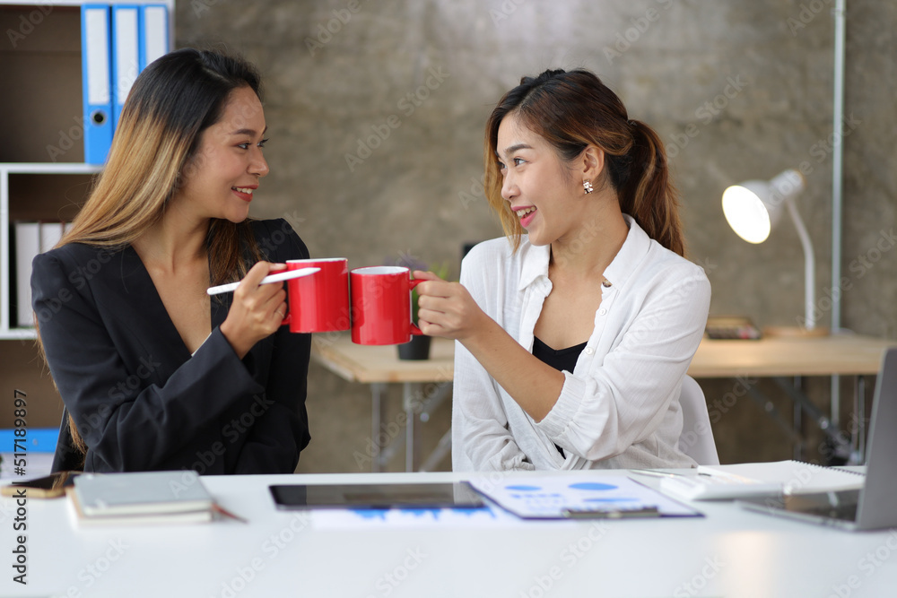 Businesswoman and coworker happily working together and drinking coffee in the office in the morning