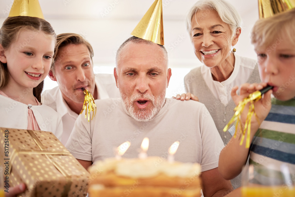 Senior man celebrating his birthday with his family at home, wearing party hats and blowing whistles