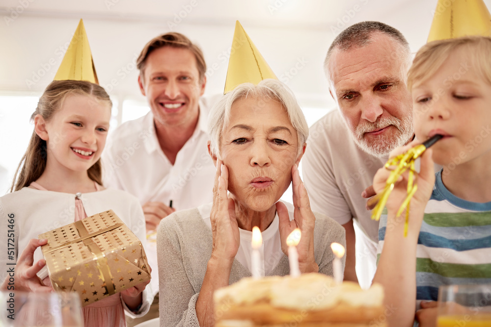 老年妇女戴着派对帽，吹着口哨，在家与家人庆祝生日。Gr