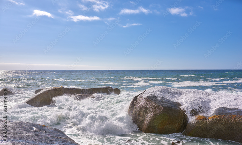 Copy space ocean view of beach with rocks, boulders and sea water washing onto rocky shore on peacef