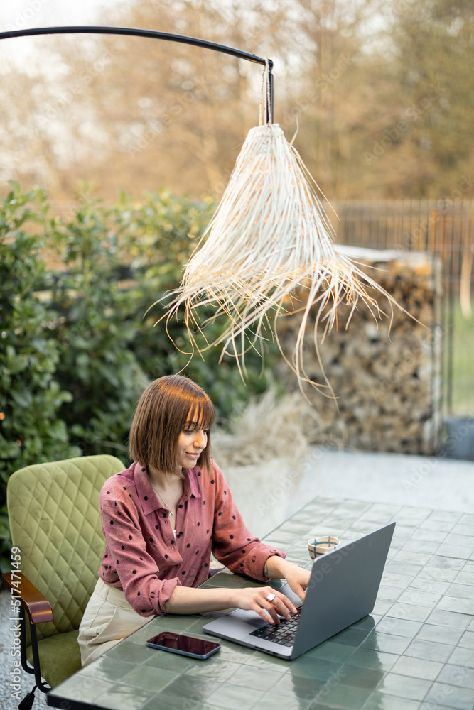 Young woman works on laptop at outdoor workspace in the garden. Concept of remote work from comforta