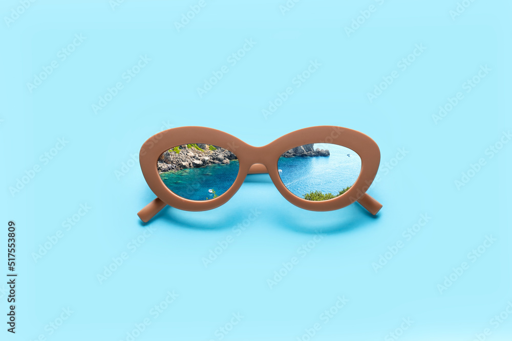 Stylish sunglasses with reflection of sea and mountains on blue background