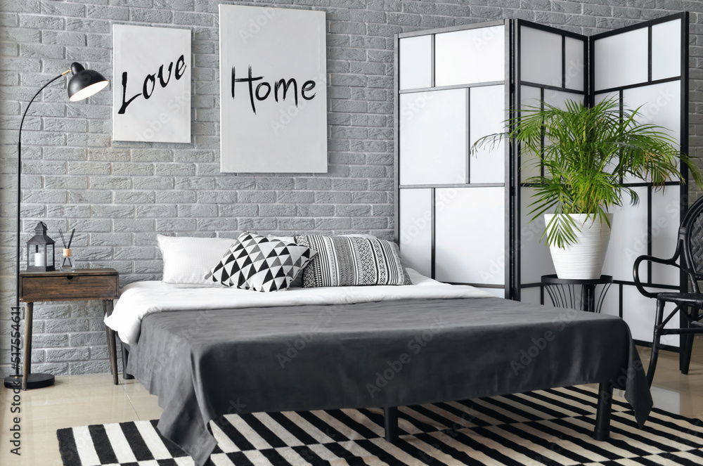 Interior of stylish bedroom with posters, lamp and folding screen