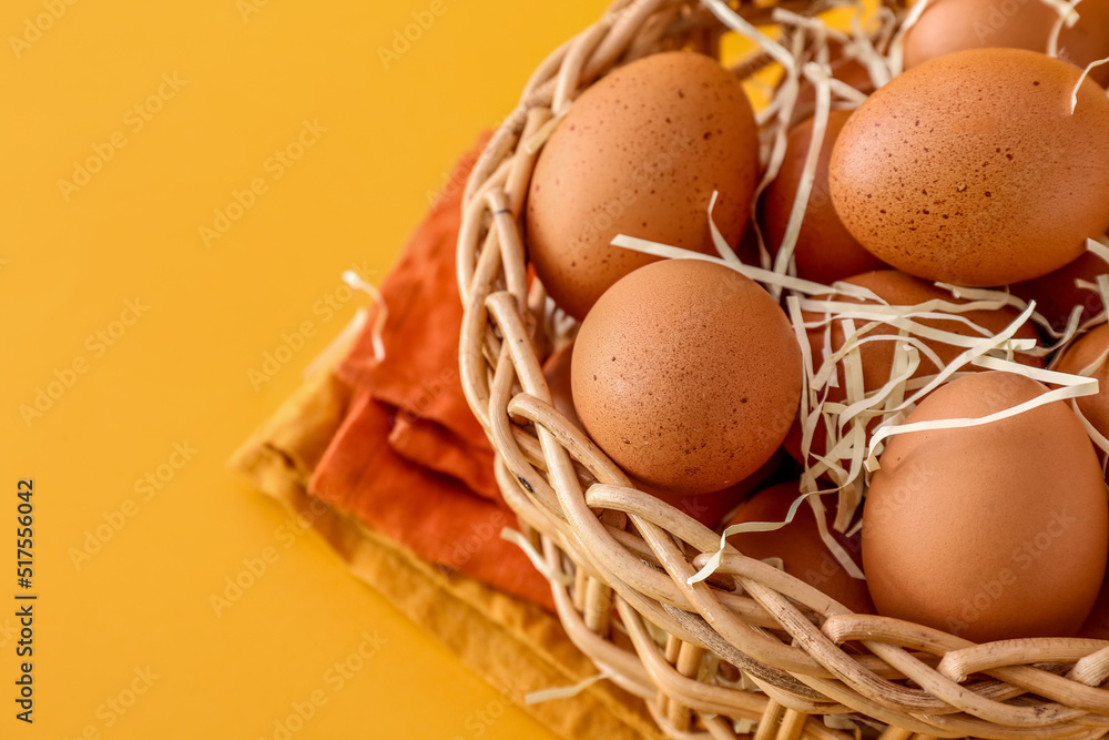 Wicker basket with brown chicken eggs on color background, closeup