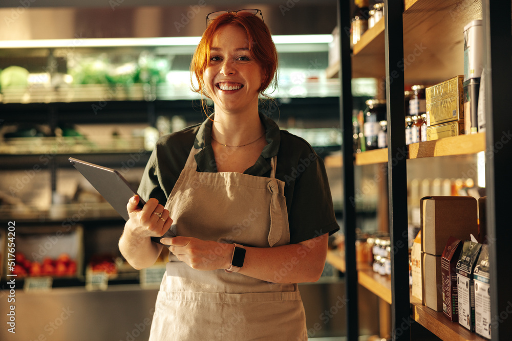 Happy young grocery store owner smiling at the camera in her shop