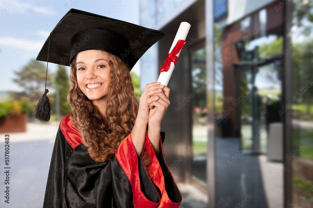 Happy young beautiful graduate female student with University degree standing and holding diploma