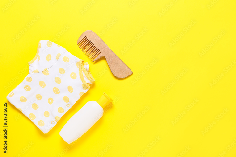 Baby bodysuit, wooden hair comb and bottle with cosmetic product on yellow background