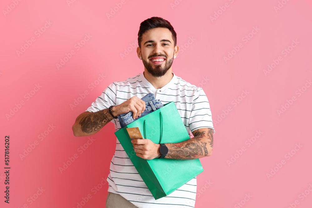 Handsome man with shopping bag and new clothes on pink background