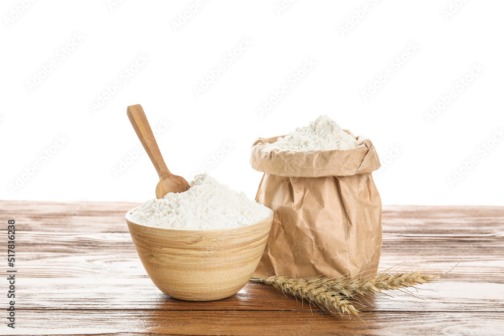 Bowl, paper bag with flour, scoop and wheat ears on wooden table against white background