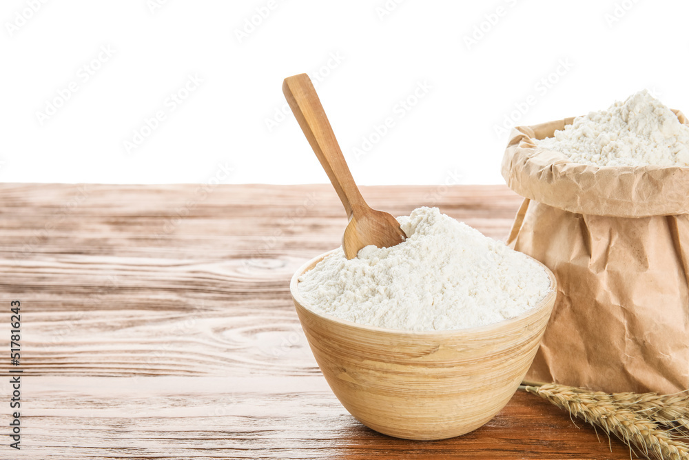 Bowl, paper bag with flour, scoop and wheat ears on wooden table against white background