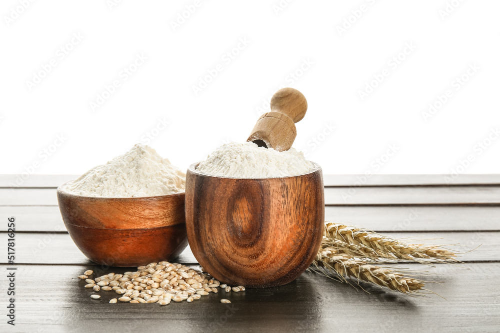 Bowls with flour, scoop and wheat ears on wooden table against white background