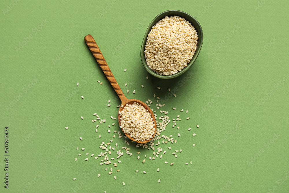 Bowl and wooden spoon with sesame seeds on green background