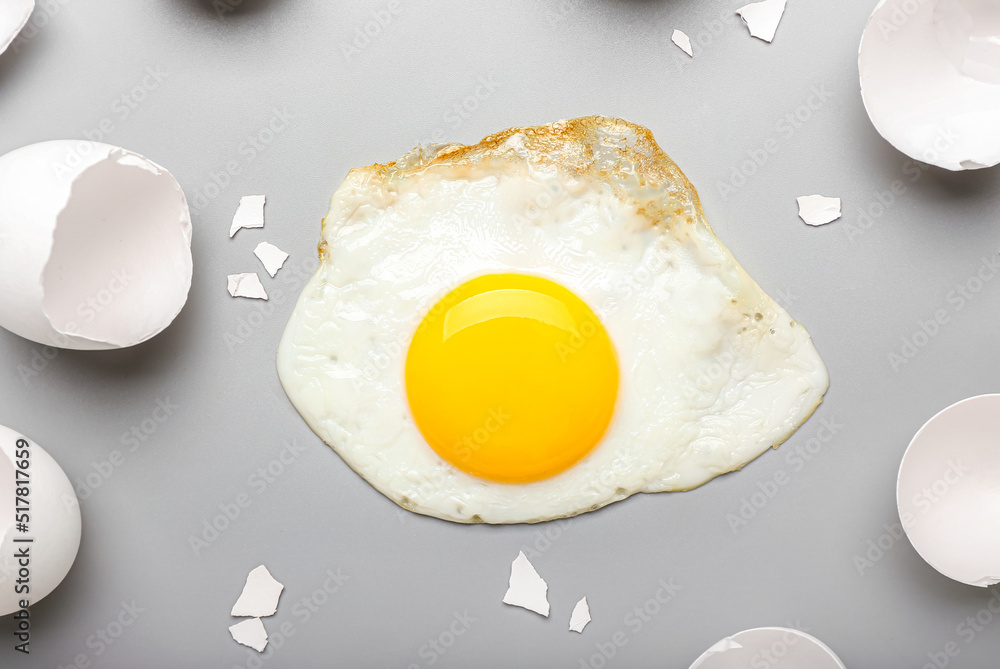 Composition with tasty fried egg and shells on light background