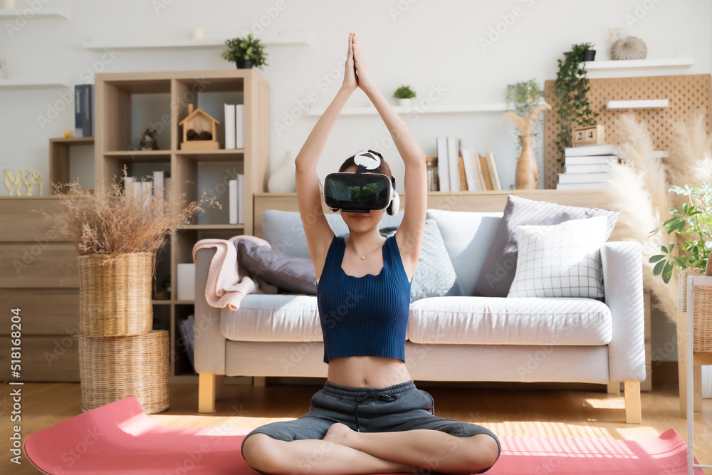 Young Asian female doing yoga in VR glasses at home