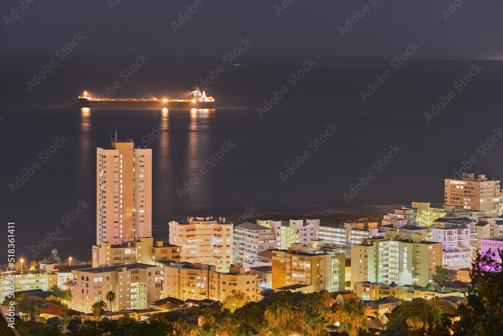 摩天大楼和城市建筑在夜晚照亮黑暗的天空，沿着海洋地平线