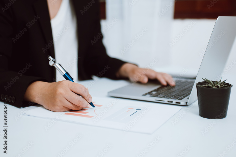 Close-up of businesswoman or accountant holding pen working with document and laptop computer on the