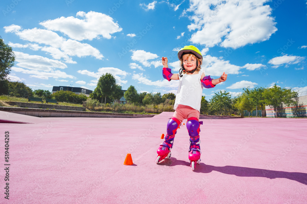 Little girl in helmet and protection learn to skate on rollers