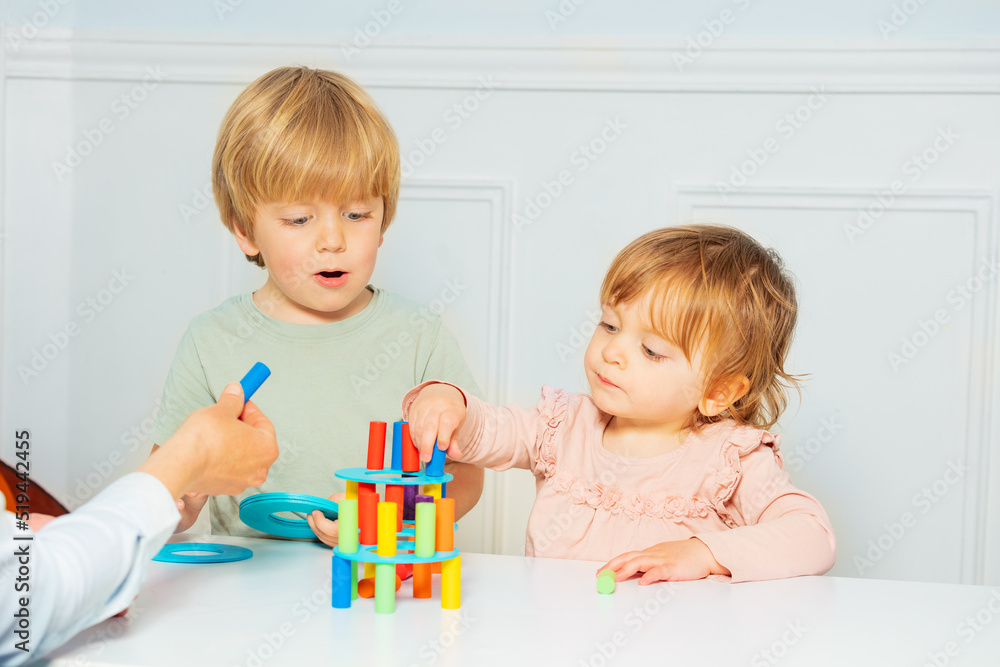 Cute boy and girl build with help of adult tower on the table