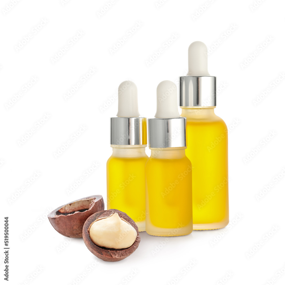 Bottles of essential oil and macadamia nuts on white background