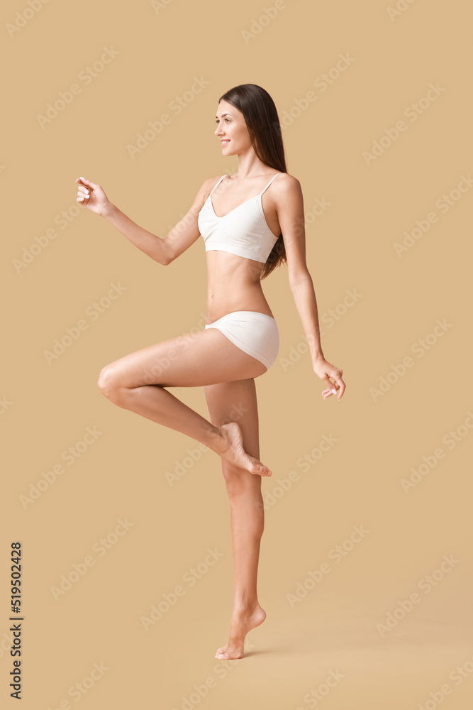 Young tanned woman in underwear on beige background