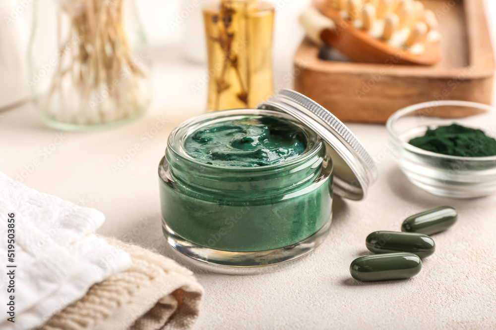 Jar of spirulina facial mask and pills on light table