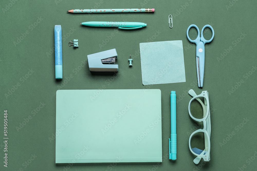 Stapler with different stationery supplies on green background