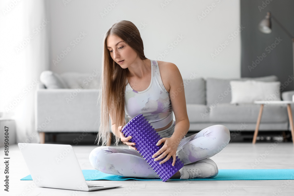 Young woman with foam roller and laptop at home