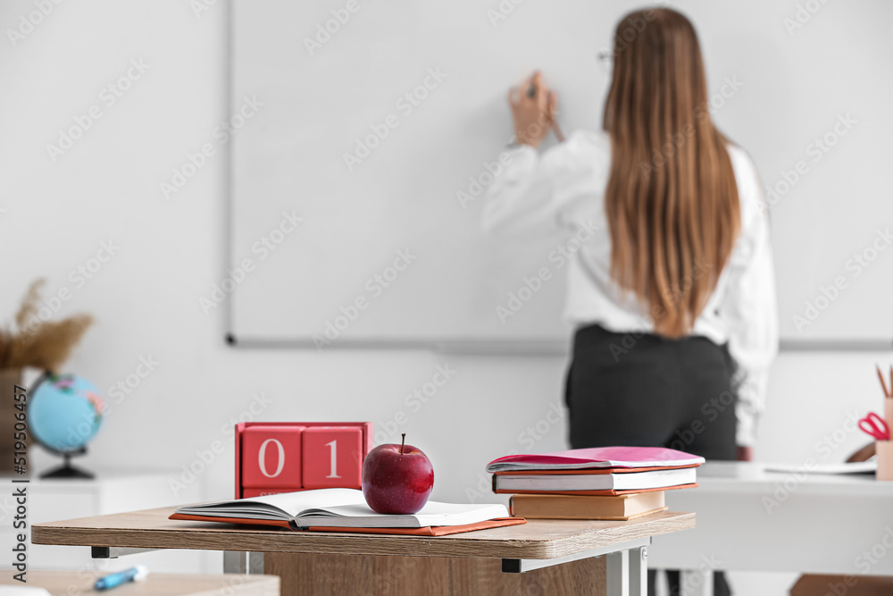 Cube calendar with date 1 SEPTEMBER, apple and school books on table in classroom