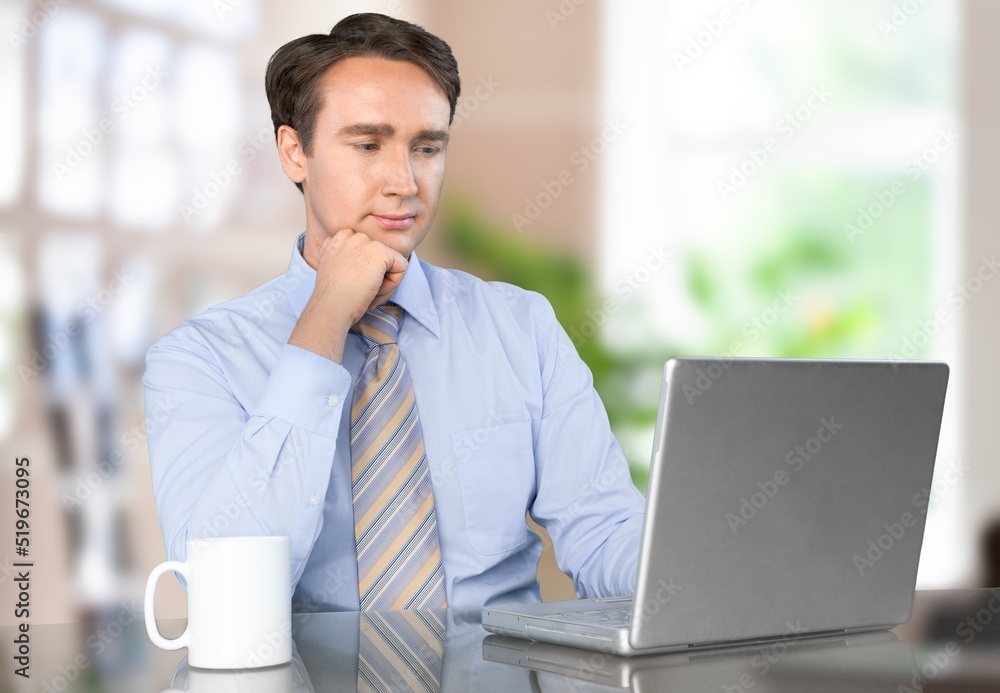 Young businessman using laptop computer in office, thinking. Happy middle aged man, entrepreneur wor