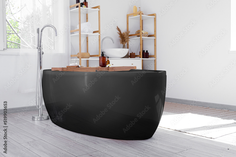 Interior of stylish bathroom with black bathtub and shelf units