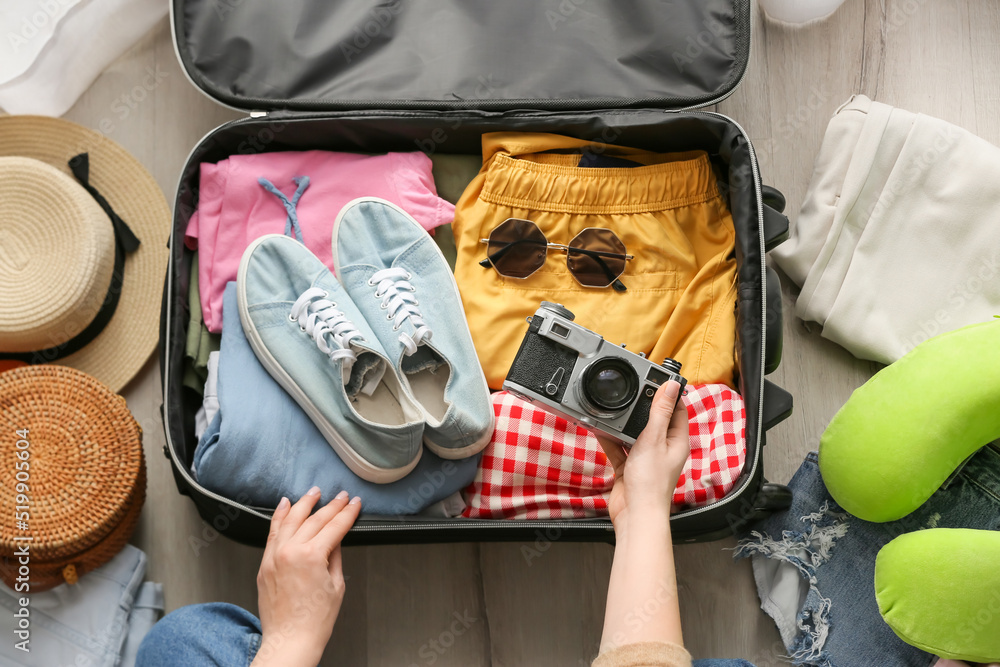 Woman putting photo camera into suitcase with traveler accessories