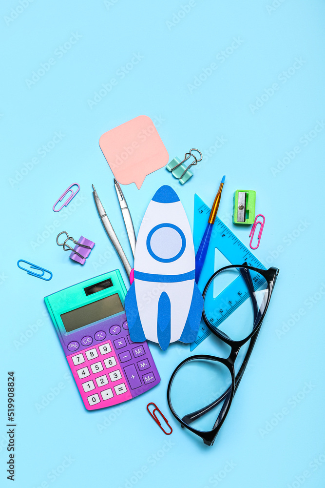 Paper rocket with school stationery and eyeglasses on blue background