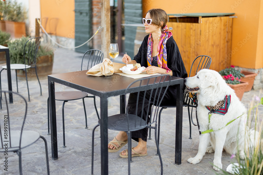 Woman tasting cheese and wine sitting with her dog at local farm shop in Maremma region of Italy. Co