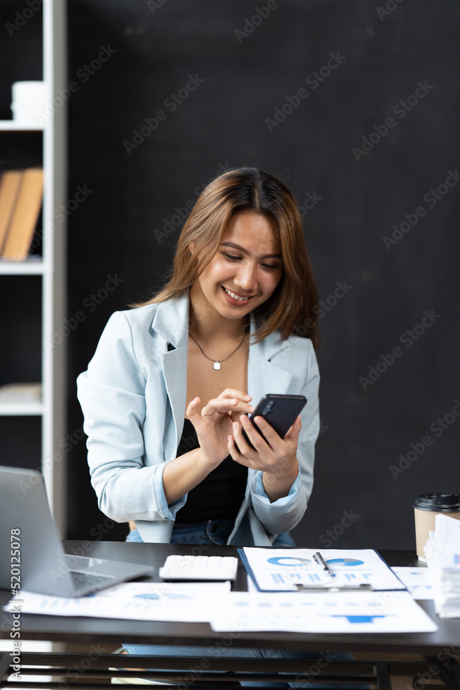 穿着正式西装的亚洲女商人在办公室里，在使用智能手机和工作时快乐快乐。