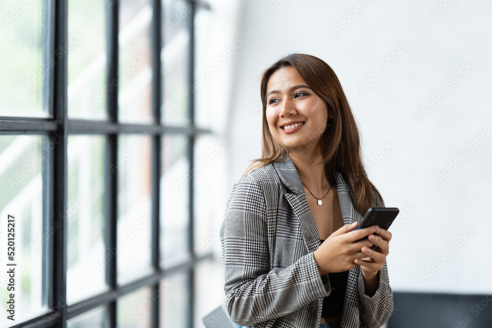 办公室里穿着正式西装的亚洲女商人在使用智能手机和工作时既快乐又愉快。