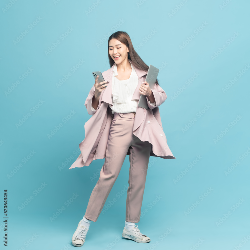 Young beautiful asian woman with smart casual cloth wearing pink coat smiling holding smartphone and