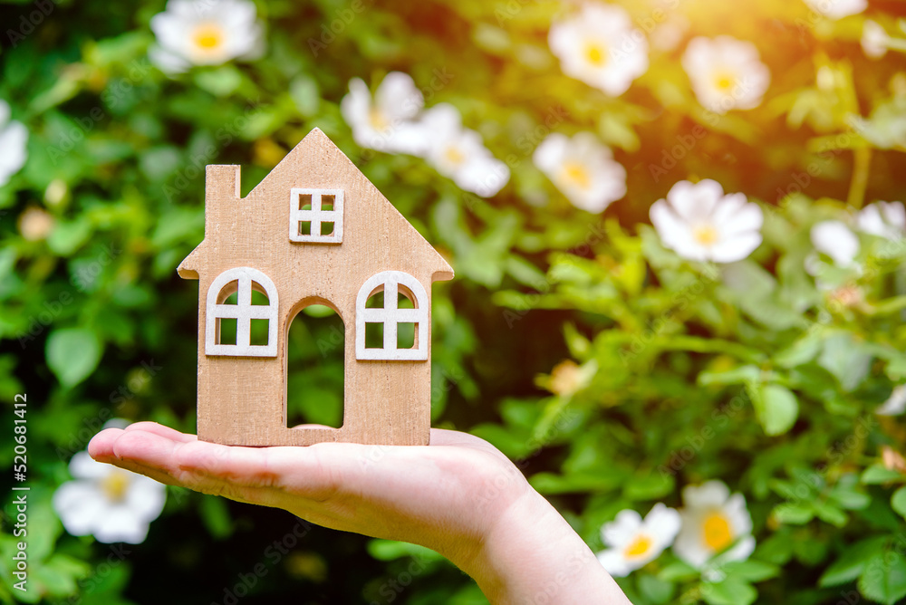 The girl holds the house symbol against the background of blossoming white rosehip
